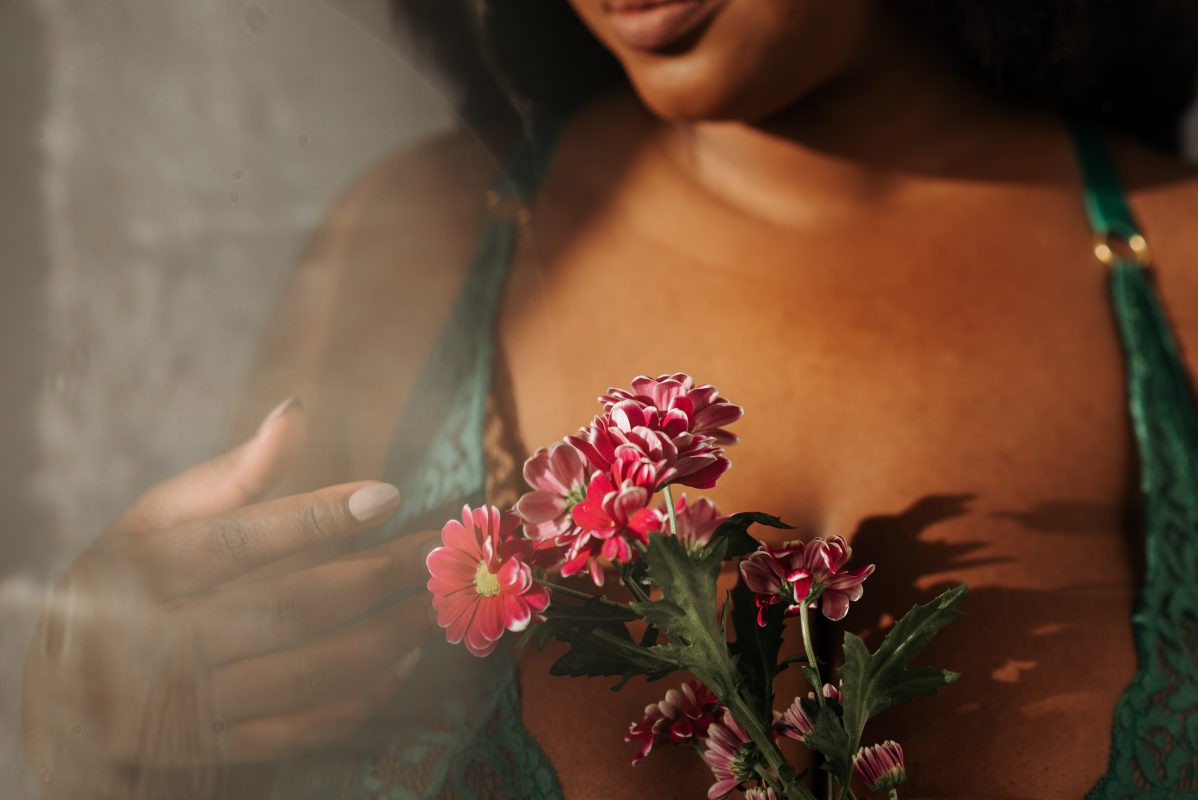 donkere vrouw in groene lingerie met rode bloemen in haar hand